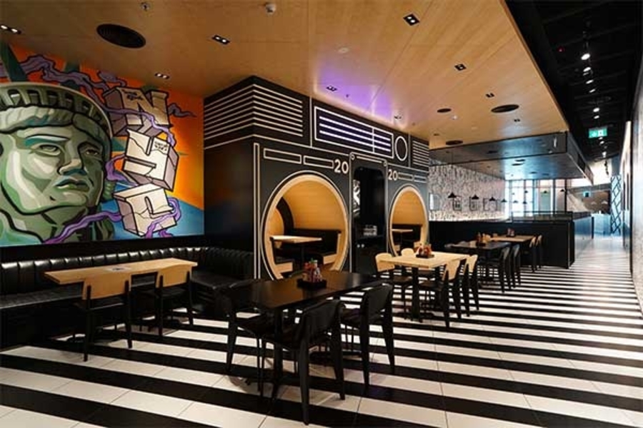 A Restaurant embellished with white and black details, art painted walls, furnished with bespoke upholstery and dining tables.